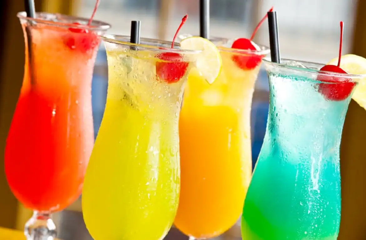 Four colorful tropical cocktails in hurricane glasses with cherries and citrus