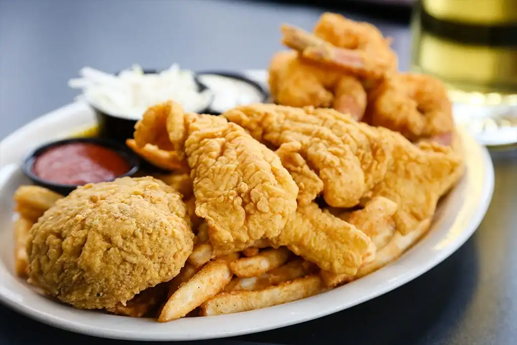 Fried seafood platter with fried fish, shrimp and a crab cake, fries, coleslaw and dipping sauces